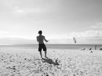 Rear view of man playing with kite at beach