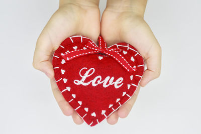 Close-up of woman's hands holding felt heart against white background