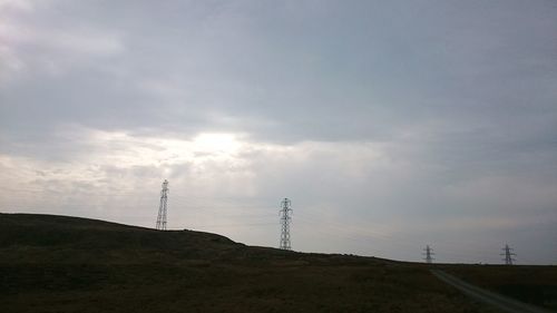 Electricity pylon on field against cloudy sky