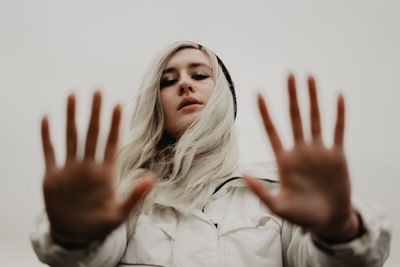 Portrait of young woman against white background, girl facing hands in the camera, wind in the hair