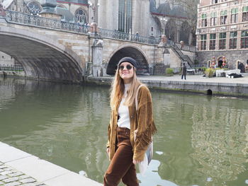 Young woman standing by canal against bridge