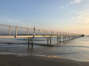 Pier on beach against sky during sunset