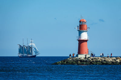 Lighthouse by sea against clear blue sky