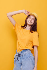 Portrait of teenager girl standing against yellow background