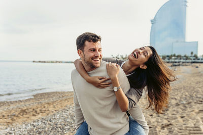Smiling man giving piggyback ride to cheerful woman at beach