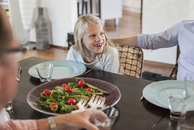 Happy girl having lunch with family at dining table