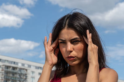 Woman touching forehead in pain against sky