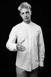 Portrait of young man standing against black background