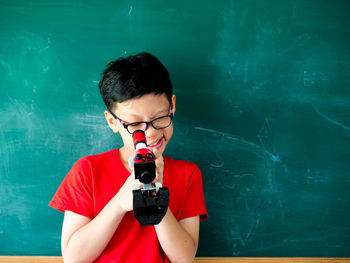 Portrait of boy wearing eyeglasses while holding against black board