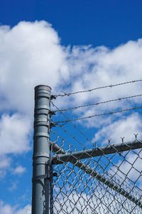 Low angle view of fence against cloudy sky