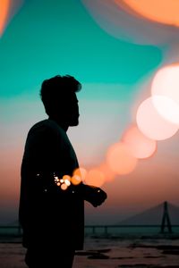 Silhouette man standing against defocused light during sunset