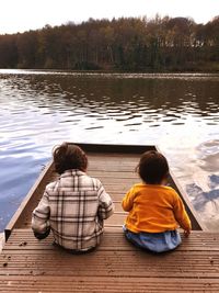 Rear view of siblings sitting on pier over lake