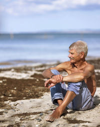 Elderly man in jeans sitting on sandy beach