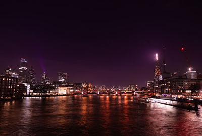 Illuminated city by river against sky at night