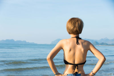 Rear view of young woman standing at beach against clear sky