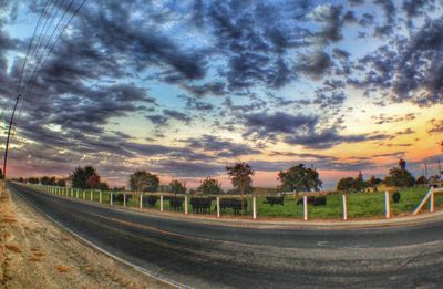 Road passing through landscape against cloudy sky at sunset