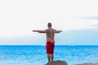 Rear view of shirtless man standing at beach against sky