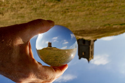 Close-up of hand holding lensball upside down against a church 