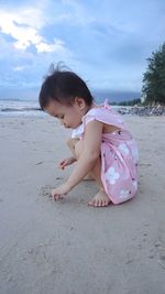 Cute girl playing in sand at beach against sky