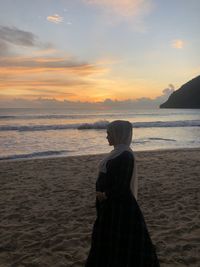 Side view of woman in hijab looking away while standing at beach