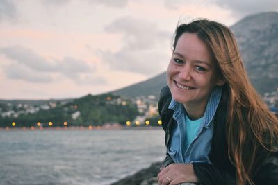 Portrait of smiling woman against river during sunset