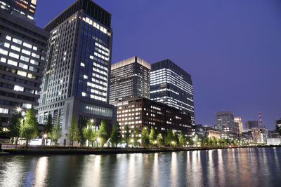 Illuminated buildings in city against clear sky at night