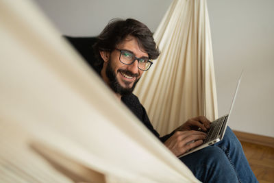 Young man  black glasses working with laptop on a white hammock notebook for working. home office