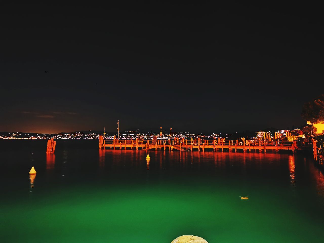 ILLUMINATED BUILDING BY RIVER AGAINST SKY AT NIGHT