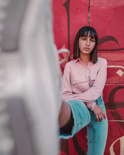 Portrait of young woman showing shoe while standing against closed door