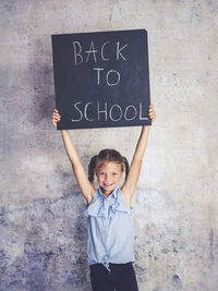 Portrait of smiling girl holding writing slate with text against wall