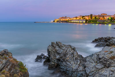 Rocks at sea shore against sky during sunrise