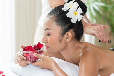 Close-up of young woman holding red petals in bowl while lying at spa