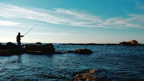 Man fishing in sea against cloudy sky