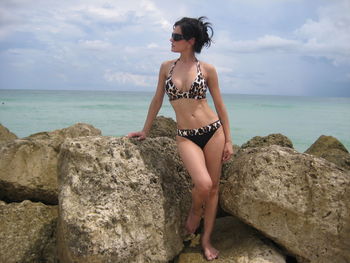 Rear view of woman sitting on rock at beach against sky