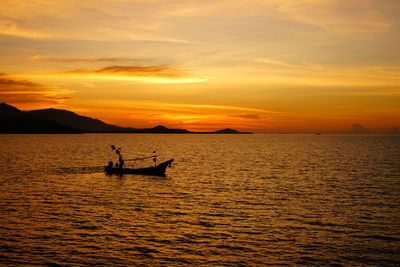 Silhouette people in boat on sea against orange sky