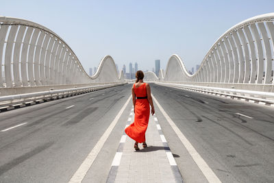 A woman in a red dress walking by an empty road on a meydan bridge with city view on background 