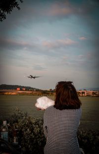 Rear view of woman standing by airplane against sky