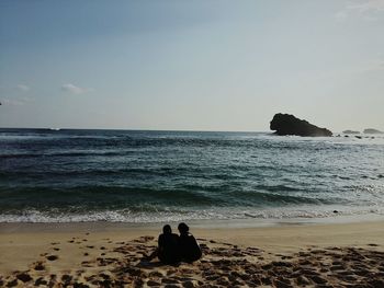 Men sitting on rock by sea against clear sky