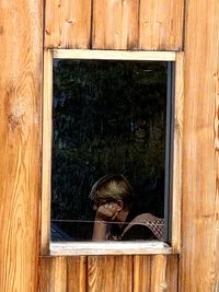 Senior woman sitting at home seen through window