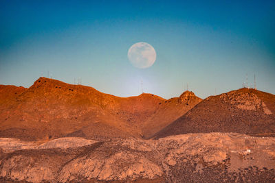 Scenic view of arid landscape against blue sky with full moon