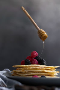 Levitating honey dipper pouring raw honey over homemade crepes on table, dark food photography