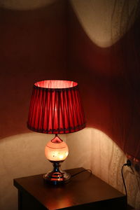 Illuminated lamp on table against wall