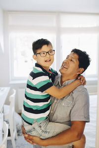 Happy father carrying disabled son while standing at home