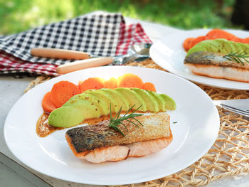 Healthy meal crispy skin salmon on white plate served with avocado and carrot slices on white table