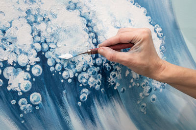 The hand of a woman artist draws an image of a sea wave using a palette knife