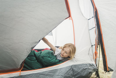 Girl in sleeping bag peeking through tent at camping site