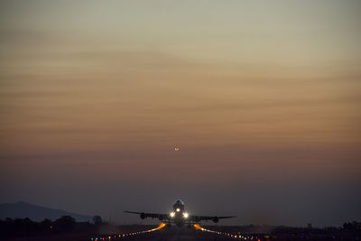 Airplane flying at runway against sky during sunset