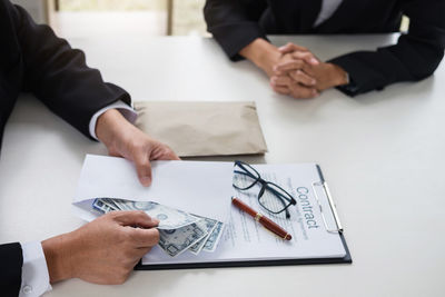 Midsection of businessman paying money to client by contract paper on desk