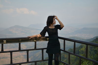 Woman looking away while standing against railing and mountain