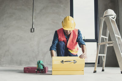 Architect holding container while crouching on floor at construction site